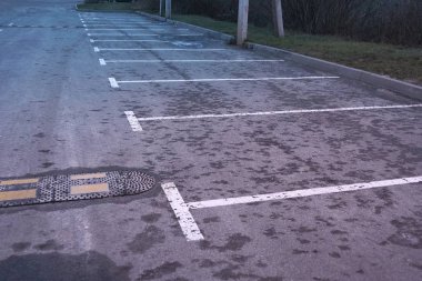 Gri ıslak asfalt park alanında beyaz işaretler ve akşam caddesinde hız tümseği var.