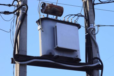 Gökyüzüne karşı iki gri beton sütun üzerinde elektrik kabloları olan büyük bir demir trafo.