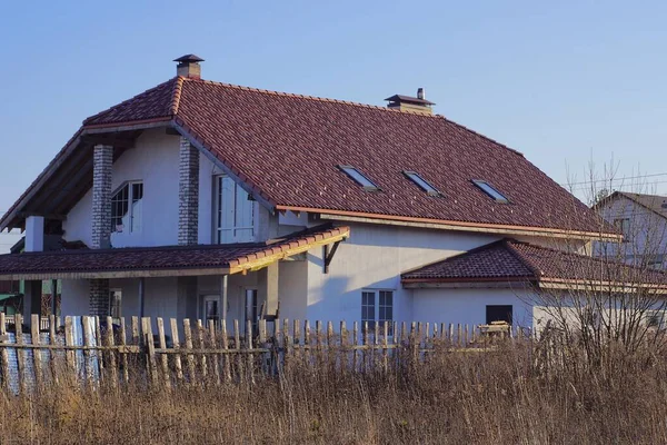 一间白色的大房子 在褐色的砖瓦屋顶下 窗户靠着蓝天 后面是灰色干草的木制篱笆 — 图库照片