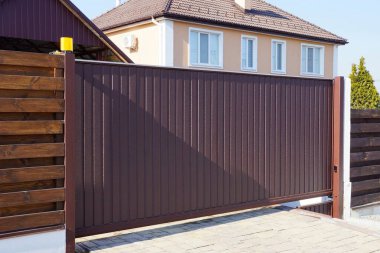 Büyük, kahverengi bir demir kapı ve kırsal bir sokaktaki ahşap bir çitin parçası.