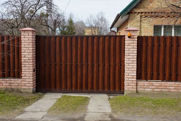 棕色关闭的私人大门和由木板和砖块构成的篱笆的一部分 在一条绿草丛中的乡村街道上 — 图库照片