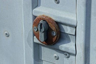 Gri metal bir kapının üzerinde paslanmış eski bir demir anahtar deliği.