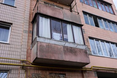 Duvarda kapalı kahverengi bir balkon ve caddede büyük bir apartmanın camları var.