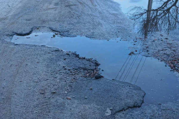 large pothole with dirty water and a puddle on the gray asphalt of the road