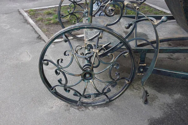 an iron wheel with a forged pattern on a decorative wagon stands on gray asphalt on the street