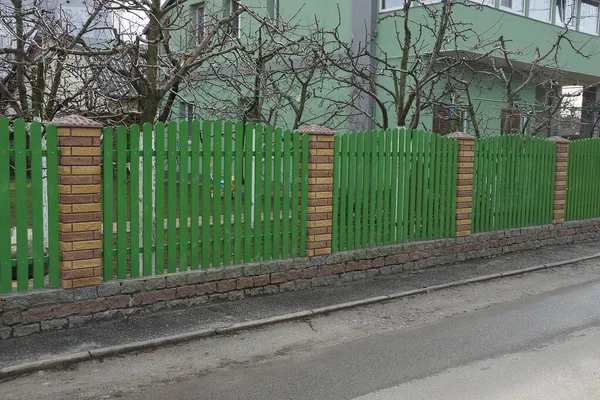 一条灰色沥青路面旁边的街道上的绿色木板和棕色砖构成的长长的私人围栏 — 图库照片