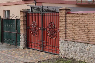 Kapalı kırmızı demir kapı, siyah dövmeli ve güneşli bir günde sokağın kahverengi tuğlalı duvarı.