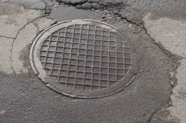 Caddedeki kaldırımda gri, nemli bir lağım çukuru var.