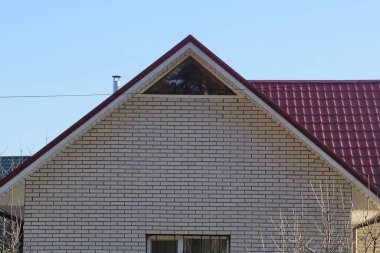 Mavi gökyüzüne karşı kırmızı kiremitli çatının altında penceresi olan özel bir evin beyaz tuğlalı dairesi.