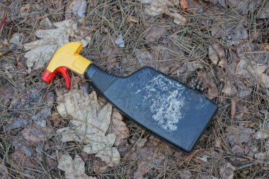 Kirli bir siyah plastik sprey şişesinin çöpü kuru gri çimlerin üzerinde uzanıyor ve parktaki doğal yaprakların üzerinde.