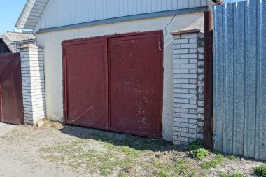 Kırmızı metal kapısı ve sokakta çiti olan beyaz bir garaj.