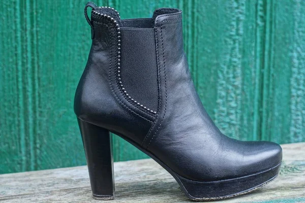 one black leather woman shoe is on a gray table against a green wall