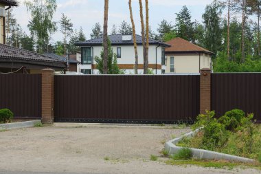 Büyük kapalı demir kahverengi kapılar ve gri asfalt üzerinde çitin bir kısmı ve sokakta yeşil çimenler