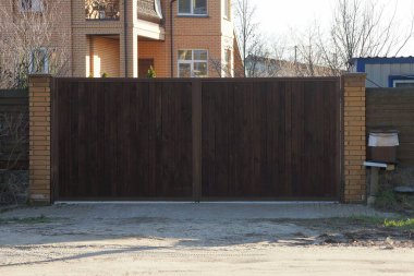 Kapalı kahverengi kapı ve sokaktaki tahta ve tuğlalardan çitin bir kısmı.