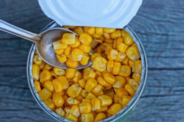 Sarı konserve mısır ve gri bir masada küçük metal bir kaşık.