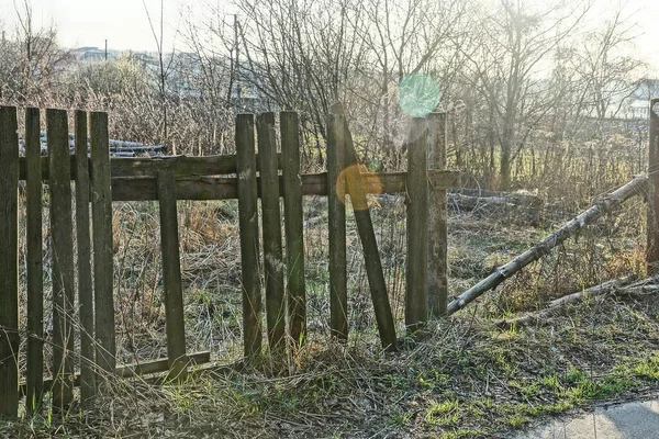 日当たりの良い日に屋外の草の中に壊れた灰色の板を持つ古い田舎の木製のフェンス — ストック写真