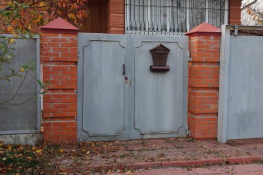 Eski gri demir kapı ve kırsal bir sokakta kırmızı tuğla ve metalden oluşan bir çitin parçası.