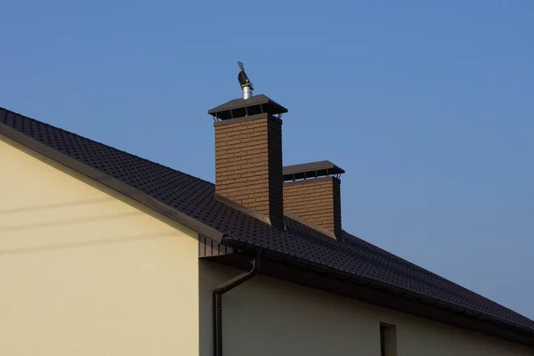 晴れた日に青い空を背景に民家の瓦屋根の上に茶色のレンガ造りの煙突が2つ — ストック写真