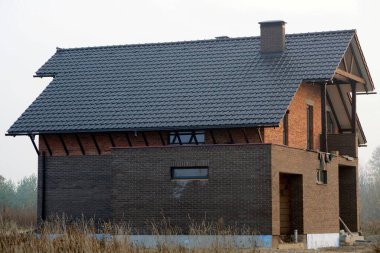 Gökyüzüne karşı kiremitli çatı altında pencereleri olan büyük kahverengi tuğlalı özel bir ev.