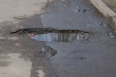 büyük bir çukur, su birikintisi ve kirli su ile bir şehir caddesinde gri asfalt üzerinde