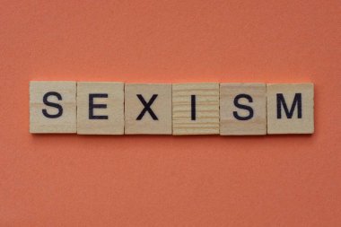 text from the word sexism from square wooden letters in black font lies on a pink table clipart