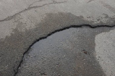 Siyah çatlamış bir yolda gri ıslak asfaltın taş dokusu.