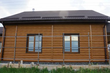 Kırsal bir sokakta fayanslı bir çatı altında iki penceresi olan kahverengi ahşap bir evin ön cephesi.