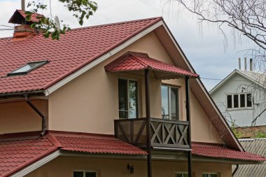 Kırmızı kiremitli çatının altında açık ahşap kahverengi balkonu olan özel bir evin tavan arası.