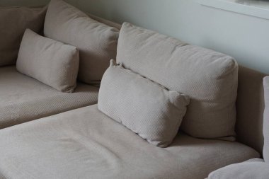 Kahverengi yastıklar büyük bir kanepede, gri bir duvarın karşısında.