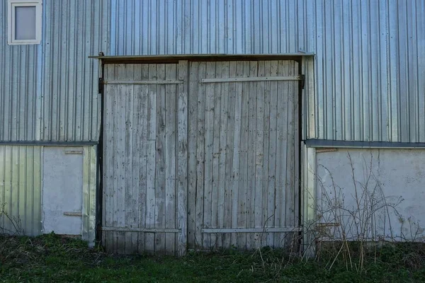 facade of an old garage with a metal wall and gray closed wooden gates in the green grass on the street