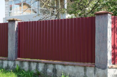 Kırmızı metal ve gri beton sütunlardan oluşan bir çit. 