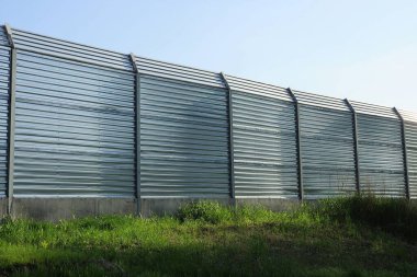 Mavi gökyüzüne karşı yeşil çimlerde yüksek gri metal çit duvarı