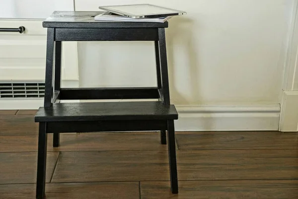 一个黑色的木制凳子靠着房间里褐色地板上的灰色墙壁站着 — 图库照片