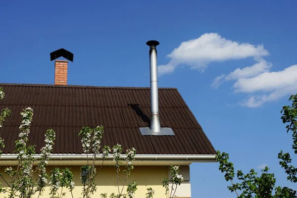 青い空に対して家の茶色のスレート屋根の上の灰色の金属煙突パイプ — ストック写真