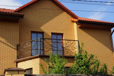 Güneşli bir günde, dışarıdaki özel bir evin kahverengi tuğlalı tavan arasında siyah, açık demir bir balkon.