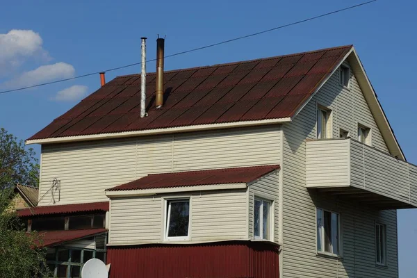青い空に対して煙突と茶色のタイル張りの屋根の下にプラスチック壁 オープンバルコニーと窓のあるグレーの民家 — ストック写真