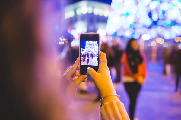 クリスマスライトの隣で女の子が別の女の子の写真を撮っている。彼らはマドリードのクリスマスライトを楽しんでいる — ストック写真