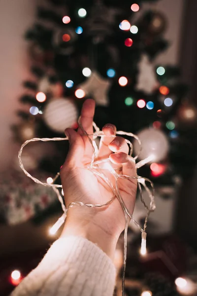 Una mano sostiene luces de Navidad frente al abeto de Navidad . — Foto de Stock