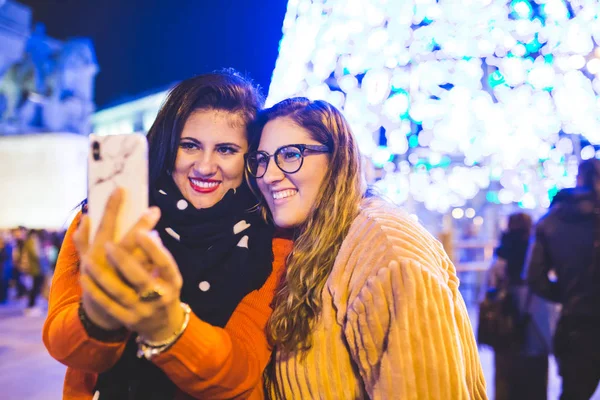 Две девушки фотографируются рядом с рождественскими гирляндами. Они наслаждаются вместе в Мадриде . — стоковое фото