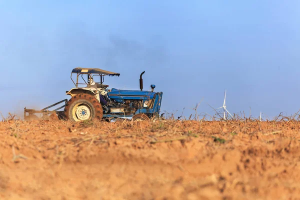 Farmer in tractor preparing farmland with wind turbine power gen — Stock Photo, Image