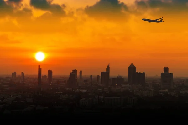 Silhouette di aeroplano che vola in un cielo sopra la città al tramonto — Foto Stock