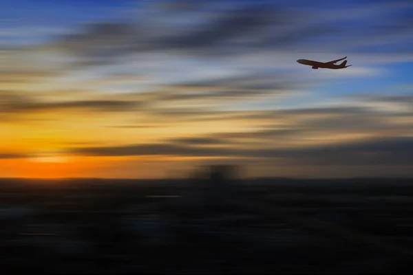 Silhueta de avião voando em um céu sobre a cidade ao nascer do sol — Fotografia de Stock