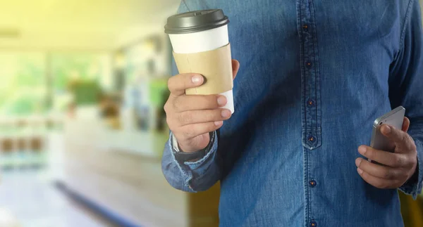 En ung man som håller en kopp kaffe på ett kafé — Stockfoto