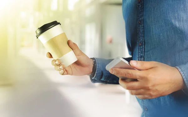 En ung man som håller en kopp kaffe med telefon — Stockfoto