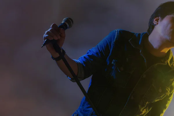 Un hombre cantando en un micrófono bajo el reflector con humo en un — Foto de Stock