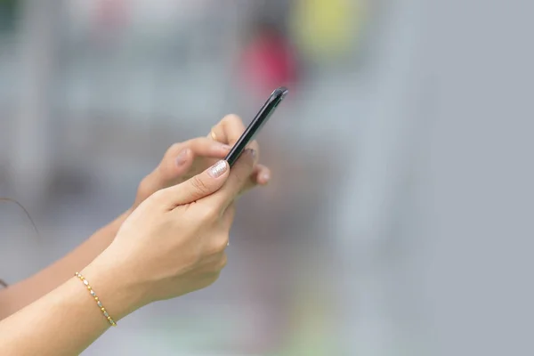 Fechar as mãos da mulher segurando telefone inteligente com backgro desfocado — Fotografia de Stock