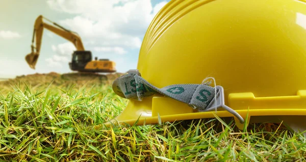 Yellow helmet and excavator working at construction site — Stock Photo, Image
