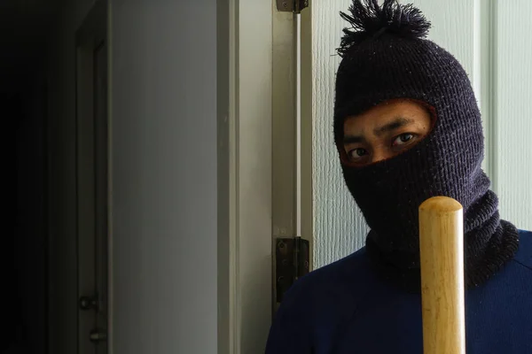 Masked robber with baseball bat hiding behind the door — Stock Photo, Image