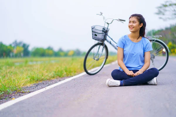 Ragazza con bici, Donna seduta sulla strada nel parco e una bicicletta — Foto Stock