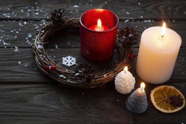 Kahverengi ahşap arka planda Noel çelengi, yanan mumlar ve çam kozalakları..